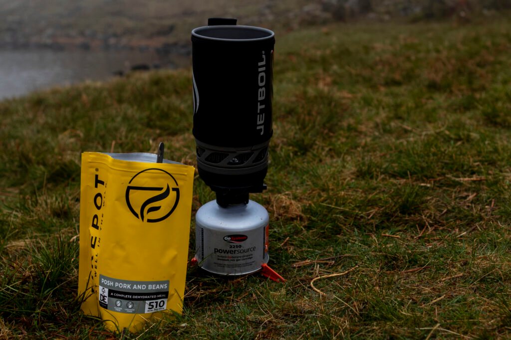 Firepot freeze-dried meal and Jetboil stove on the grass by a Lake District tarn